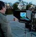 A man looks at a small screen attached to a large black piece of electronic equipment outdoors.