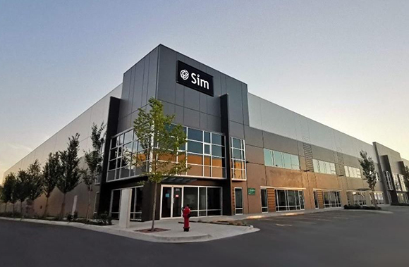 A large, multi-story gray industrial building with a black sign that reads 'Sim' under a clear sky.