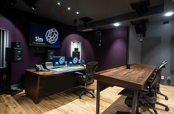 A professional recording studio featuring a mixing desk, large monitors, and a wooden conference table.