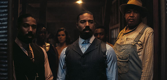 A group of diverse people looking forward in a dark, indoor setting with warm lighting.