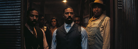 A group of diverse people looking forward with serious expressions in a dark, moody interior.