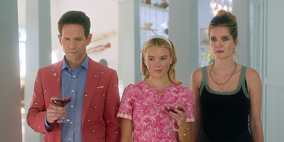 A man in a red blazer and a woman in a pink patterned top stand next to a woman in a black tank top.