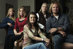 Five people, three women and two men, posing together for a group portrait in a dimly lit room.