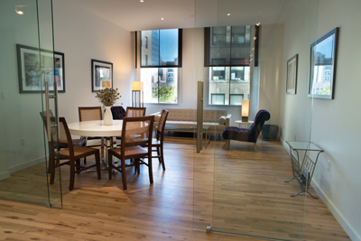 A dining table with chairs and a living area with a sofa and armchair seen through glass partitions.