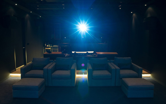 A dark home theater room with four blue armchairs and a bright blue light shining from the center.