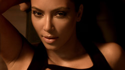 Close-up portrait of a woman with dark hair and makeup looking directly at the camera in warm lighting.