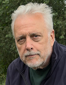 Close-up portrait of an older man with white hair, a grey beard, and blue eyes looking directly at the camera.