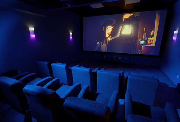 Rows of blue velvet theater seats facing a large projection screen showing an animated character.