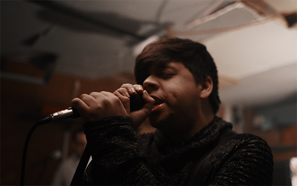 A person with dark hair singing closely into a handheld microphone.