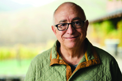 A smiling man with glasses and a green quilted shirt outdoors.