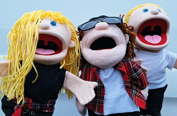 Three hand puppets with blonde and brown hair, wearing sunglasses and plaid shirts, posed together.