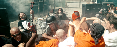 A crowd of people fighting in a brawl while a heavy metal band performs in the background.