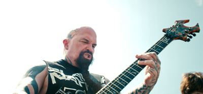 A man with a goatee and tattoos playing an electric guitar outdoors.