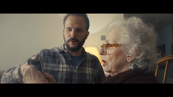 A man in a plaid shirt and an elderly woman with white hair look at a smartphone together.