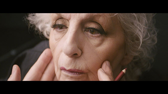 Close-up of an older woman with curly white hair resting her face in her hands.