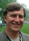 A smiling man with brown hair wearing a grey blazer and a lanyard.