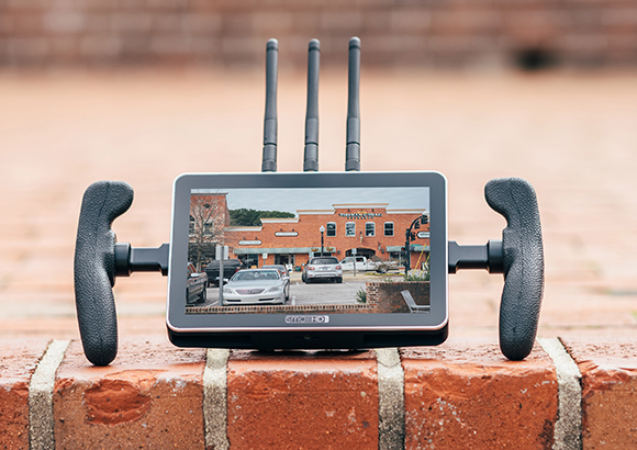 A video monitor with three antennas and two handgrips sitting on a brick ledge.