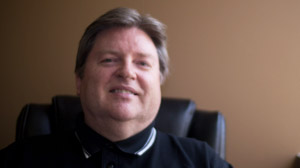 A smiling man with short brown hair wearing a black polo shirt.