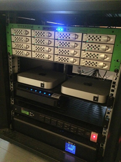 Server rack with multiple tiers of electronic devices, including a green storage array, two Apple Mac Minis, and other networ