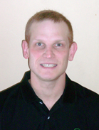 A smiling man with short reddish-blonde hair wearing a black polo shirt against a plain light background.