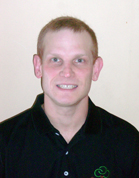 A man with short blond hair smiling at the camera while wearing a black polo shirt.