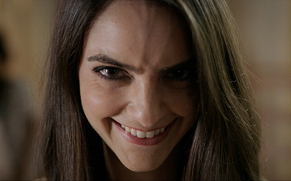 A close-up of a woman with long dark hair smiling with a wide, intense expression.