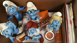 Several blue Smurf figurines with different hats and expressions inside a cardboard box with papers.
