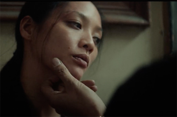 Close-up of a woman looking downward as a hand gently touches her chin.