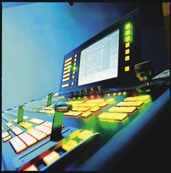 A close-up of a video production switcher console with illuminated yellow buttons and a digital display.