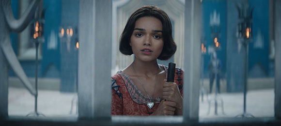 A young woman with dark hair looks through a window frame with a worried expression.