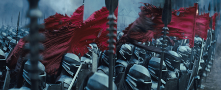 A line of soldiers in dark metal helmets holding spears and tattered red banners.