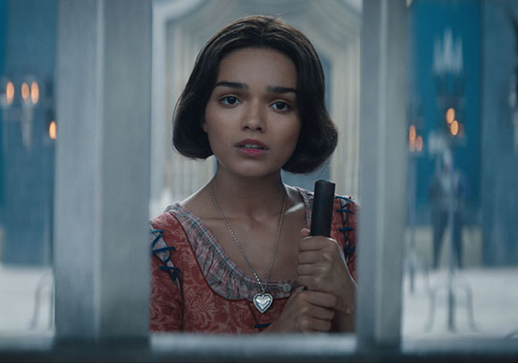 A young woman with dark hair looks through a window frame while holding a dark handle.