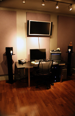 A computer desk with two monitors, a black office chair, and two large speakers on stands in a room.
