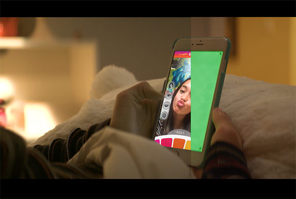 A person holds a smartphone in a dimly lit room, showing a social media interface with a selfie.