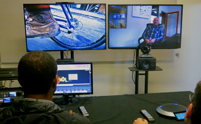 A person sits at a desk facing two large monitors and a smaller computer screen showing graphics.