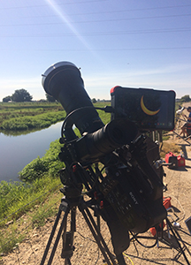 A large professional camera with a long telephoto lens mounted on a tripod by a river.