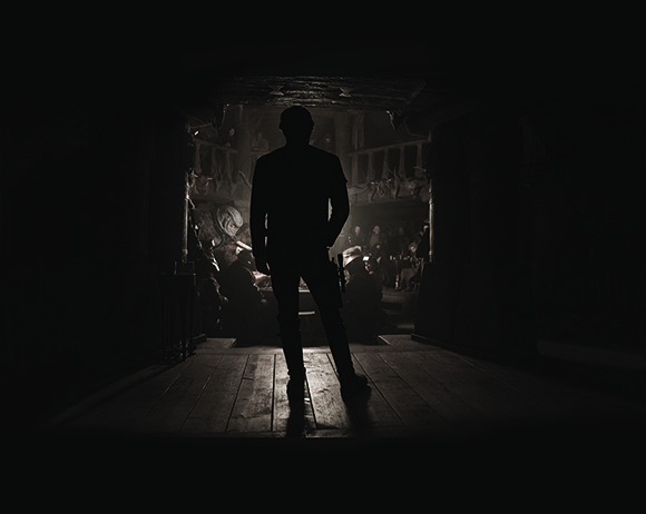 Silhouette of a man standing in a doorway looking into a dimly lit room with people.