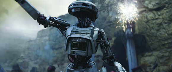 A metallic robot with a rounded head stands with one arm extended upward in a rocky environment.