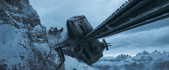 A massive metal bridge or pipeline structure stretches across a snowy, mountainous landscape under a cloudy sky.