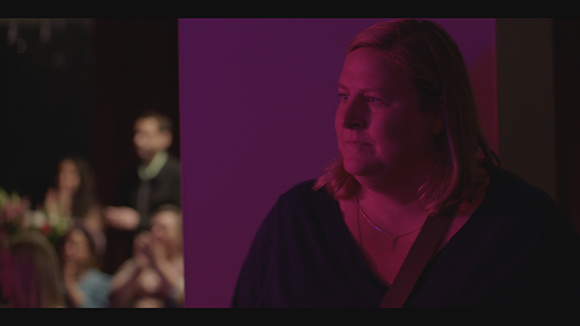 A woman with blonde hair looks to the side in a room with purple ambient lighting.