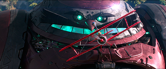 A small red biplane flies across the face of a giant, dark red mechanical robot with glowing green eyes.
