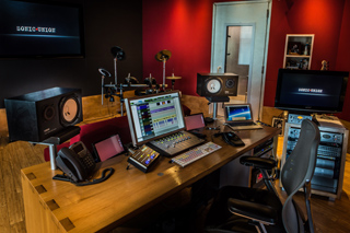 A music production studio with a mixing console, computer monitors, studio monitors, and a desk.