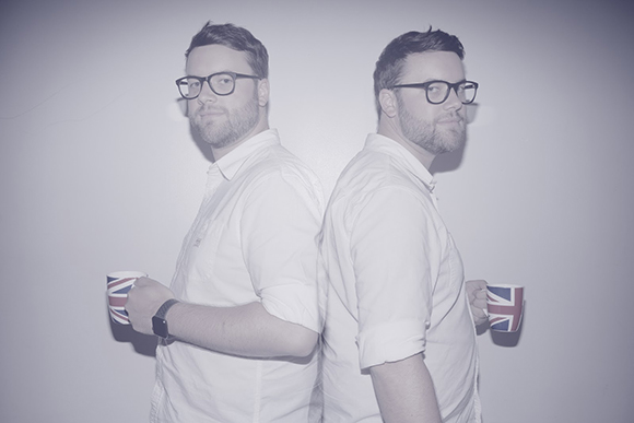 Two men in white shirts stand back-to-back holding mugs with British flag patterns.