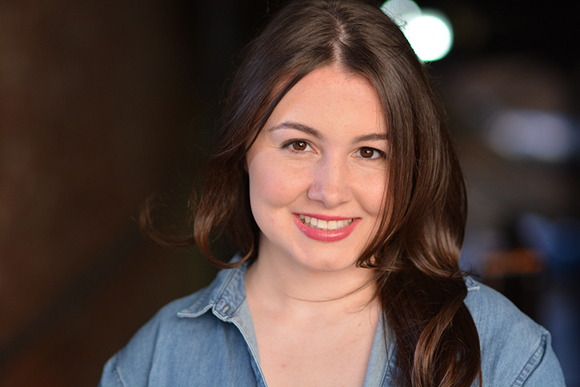 A smiling woman with long brown hair and a blue denim shirt looking at the camera.