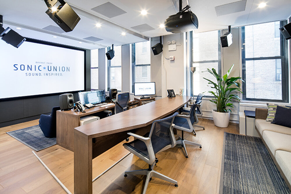 A bright conference room featuring a large projection screen, a long wooden table, and several office chairs.