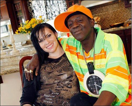 A smiling woman with dark hair and a man in an orange cap and bright striped shirt pose together.