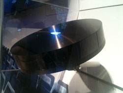 A black, circular electronic device with a glowing blue light on its surface, possibly a speaker or router.