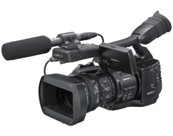 A professional black Sony video camera with a large lens hood and a shotgun microphone attached to the top.
