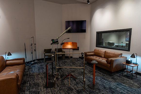 A studio space with two brown leather sofas, a television, and various metal lighting and camera stands.