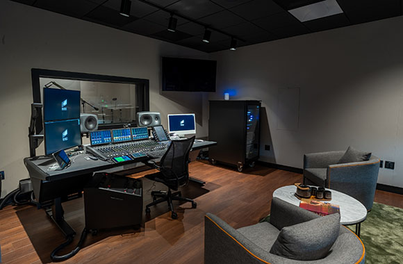 A professional recording studio featuring a large mixing console, studio monitors, and computer workstations.